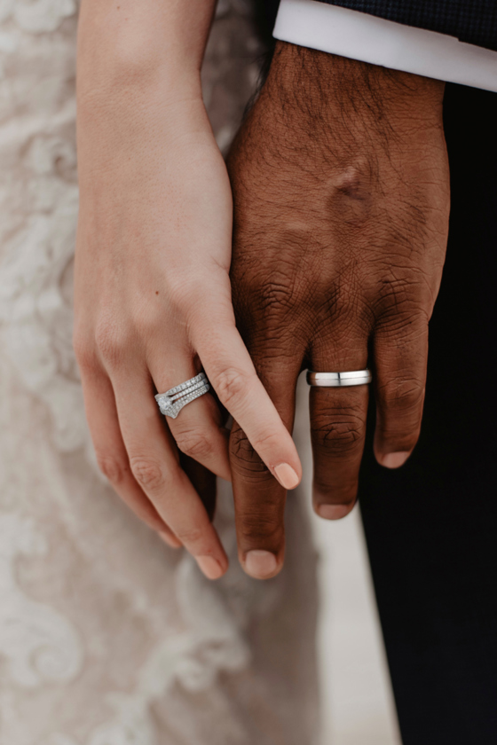 Bride and groom's hands with silver wedding rings by James Porter & Son